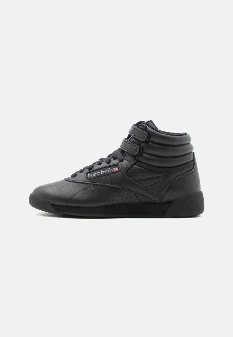 Baskets montantes Reebok noires avec deux bandes Velcro, lacets, col rembourré et logo sur le côté, sur fond blanc uni.
