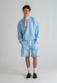 Hellblaues Sweatshirt und Shorts-Set aus weichem Material, mit lockerer Passform. Ein gemusterter Schal ist um den Hals gebunden. Schwarze Schuhe getragen.
