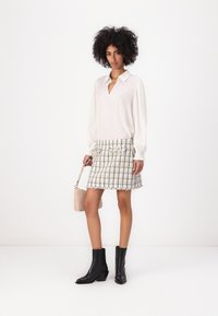 Blusa blanca con escote en V y mangas plisadas, combinada con una minifalda de tweed multicolor. Botines negros y un pequeño bolso beige.