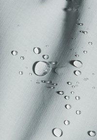 Waterdruppels parelen op lichtgrijze, gestructureerde stof, wat wijst op een waterafstotend of waterdicht oppervlak.