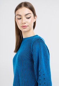 Maglione blu a coste con scollatura rotonda e motivo testurizzato. Presenta strisce scure a contrasto e dettagli lavorati a maglia sulle maniche.