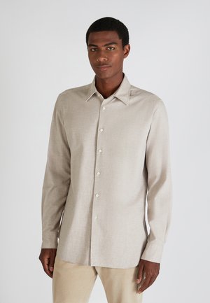 Camisa de manga larga beige claro en una tela texturizada, con cuello punta y cierre de botones en la parte delantera. Color sólido con un patrón sutil.