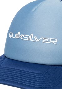 Blå keps med rundad topp och en strukturerad marinblå skärm. Har ett texturerat tyg med vit "Quiksilver"-logotyp och ribbade detaljer på skärmen.
