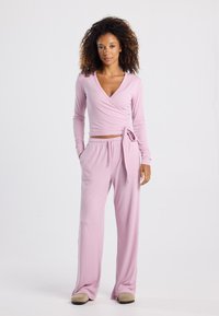 Light pink wrap top with long sleeves and a tie waist, paired with matching loose-fit pants in a soft knit fabric. Simple design, no patterns.