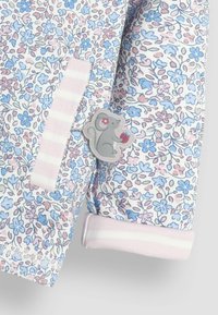 Tela con patrón floral en tonos rosa y azul que presenta un parche de un ratón gris sosteniendo fruta, con puños a rayas rosas. Material suave y liviano.