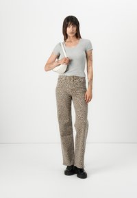 Siva prilagođeni majica, hlače visokog struka s bež i smeškim leopard uzorkom, i crne cipele s debelim đonom. Konturirani dizajn, ležeran stil.