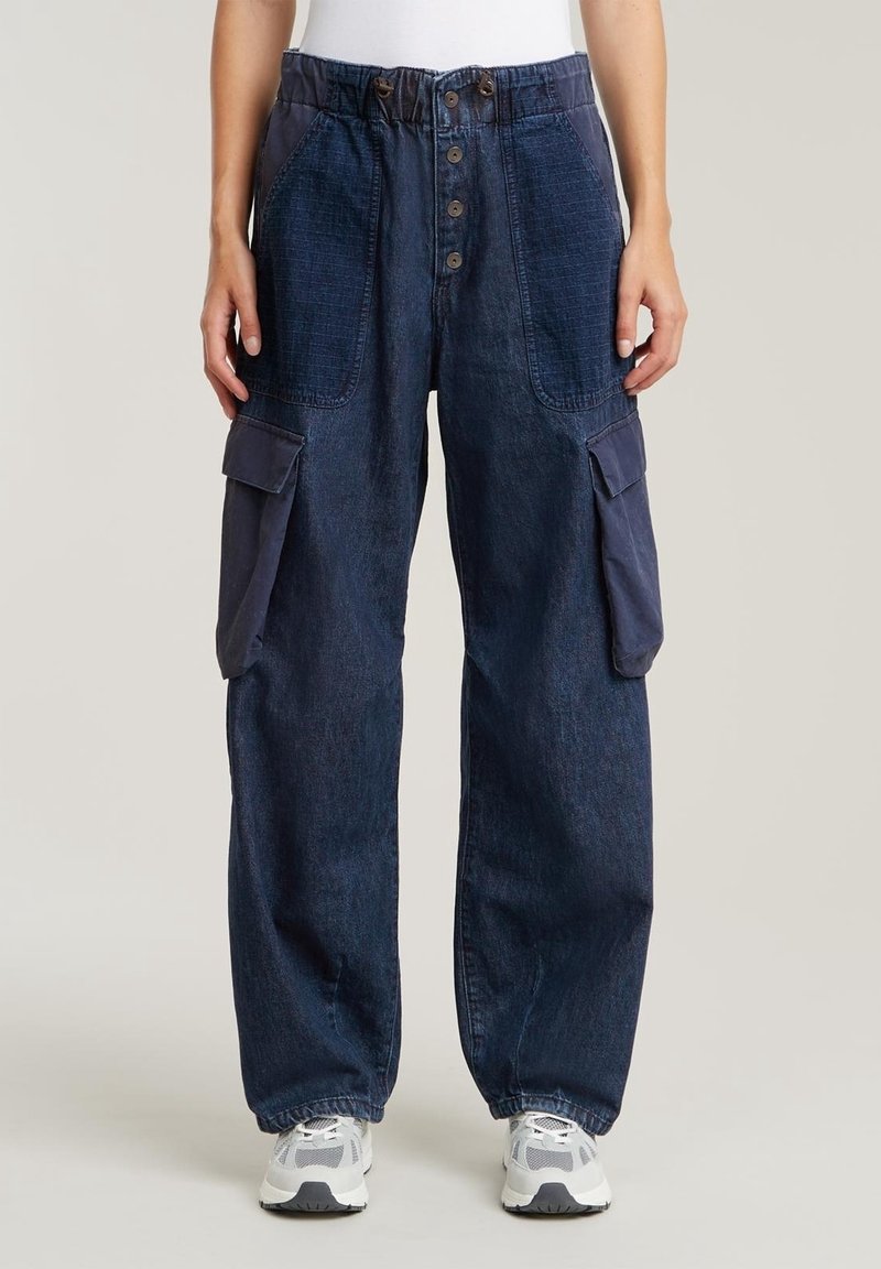 Tummansinisiä cargo-housuja rentoa istuvuutta, joissa on naru- ja vetoketjuyeritys, useita läpälaukkuja ja nappisuljenta.