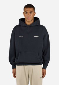 Dark navy hoodie with a front pocket, drawstring hood, and embroidered text. Features ribbed cuffs and hem, paired with light beige ribbed pants.
