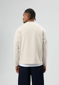 Lichtbeige sweatshirt met een ontspannen pasvorm en lange mouwen, gecombineerd met donkerblauwe spijkerbroek. Gladde textuur met een eenvoudig, ongecompliceerd ontwerp.