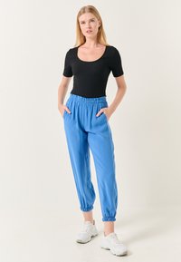 Zwarte korte mouwen bodysuit gecombineerd met blauwe, relaxte broek met elastische boorden en zijzakken, gedragen met witte sneakers.