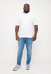 Weißes Poloshirt, blaue Slim-Jeans, graue Sneakers. Merkmale: Logo auf der Brust, kurze Ärmel und eine weiche, glatte Textur.