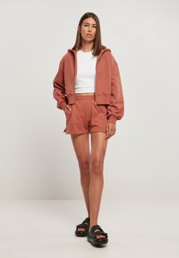 Rosa crop hoodie med glidelås, hvit t-skjorte, matchende rosa shorts og svarte sandaler med dobbel stropp. Myk tekstur, avslappet passform og enkelt design.