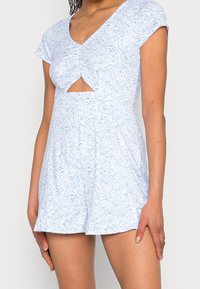 Ljusblå overall med paisleymönster, utskärning fram, och korta ärmar. Snyggt tyg, avslappnad passform och utsvängda shorts.