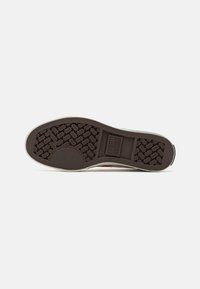 Suela de sneaker de goma marrón con un patrón texturizado, que presenta un logo central y un ribete blanco contrastante. Forma plana y redondeada.