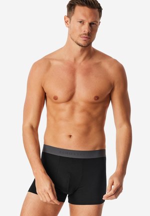 Boxers noirs avec une ceinture élastique grise arborant un logo en relief. Tissu lisse, coupe ajustée, longueur mi-cuisse.