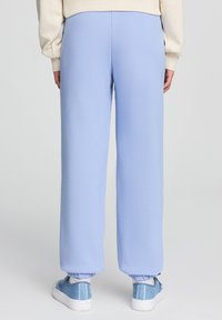 Pantaloni della tuta azzurri chiari realizzati in tessuto morbido, con cintura elasticizzata e polsini, abbinati a sneakers blu.