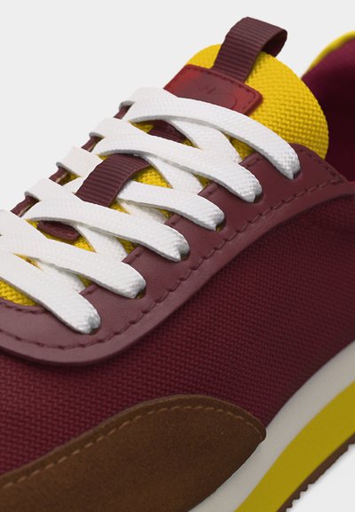 Baskets avec lacets blancs, tissu et panneaux en cuir bordeaux, languette jaune, bout en daim marron et semelle jaune et blanche.