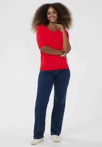 Rød kortærmet top parret med mørkeblå straight-leg jeans og lyse sko. Glat tekstur, afslappet design. Simpel sølvarmbånd.