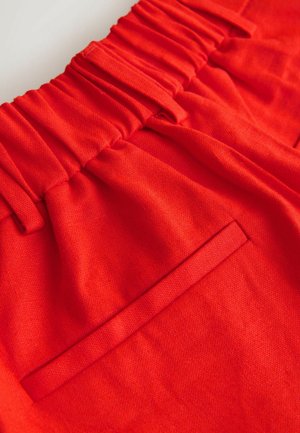 Világos piros nadrág rugalmas derékpánttal és egy kis, vízszintes hátsó zsebbel, sima anyagból.