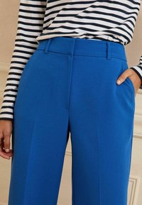 Pantalon large bleu avec une texture lisse, doté d'un devant plat, de passants de ceinture et de poches latérales. Associé à un haut rayé à manches longues.