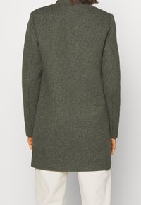 Langer dunkelgrüner Wollmantel mit einem maßgeschneiderten Design, geradem Schnitt und langen Ärmeln. Verfügt über eine glatte Textur und ein dezentes meliertes Muster.