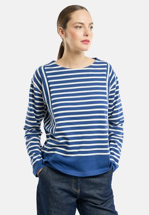 Chemise à rayures bleues et blanches à manches longues avec un col rond et un ourlet bleu uni, fabriquée dans un tissu doux et texturé. Associée à un jean.