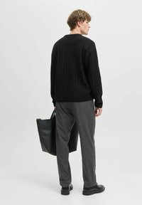 Schwarzer gerippter Strickpullover, lockere Passform, runder Halsausschnitt. Kombiniert mit grauen, maßgeschneiderten Hosen und einer schwarzen Tragetasche, vor einem neutralen Hintergrund.
