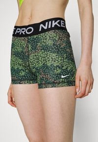 Shorts de sport à motifs verts avec une taille noire portant "Nike Pro" en blanc. Présente un design floral et un logo Nike brodé.