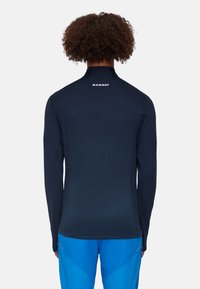 Marineblaues Langarm-Performance-Oberteil mit hohem Kragen, gerippter Textur und dem "Mammut"-Logo auf der Rückseite, kombiniert mit blauen Sporthosen.