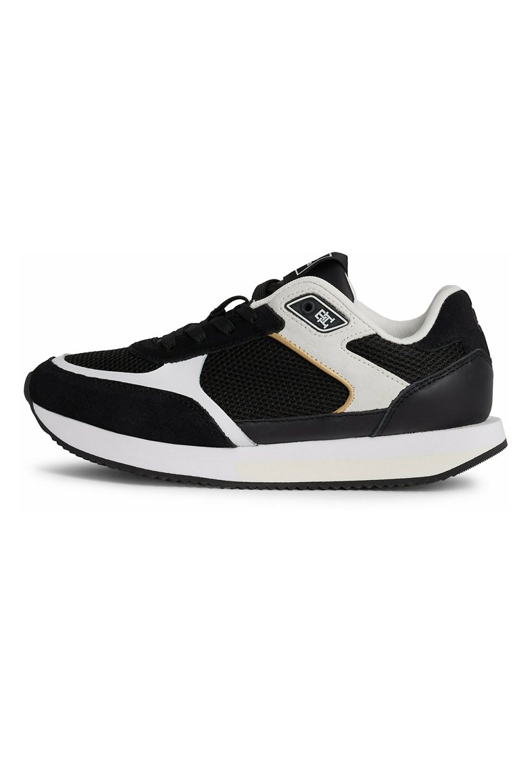 Zapatilla deportiva en blanco y negro con parte superior de malla, acentos de ante, cuello acolchado y suela de goma con un patrón texturizado.