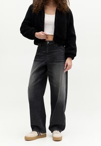Black, fleece bomber jacket over a white cropped top; paired with high-waisted, loose-fit, dark gray jeans and light sneakers with tan soles.