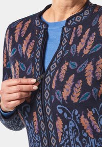 Sweater zippé marine avec des motifs colorés de plumes et de fleurs en orange, bleu et vert, doté d'un col rond et d'un tissu tricoté texturé.