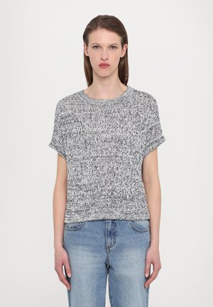 Kortermet, svart-hvitt flekket strikkegenser med rund hals og avslappet passform, kombinert med lyseblå denimjeans.