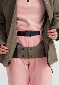 Bruine gestructureerde jas over een roze fleece top, gecombineerd met roze broek. Bevat een zwarte verstelbare riem en drukknoopsluiting op de jas.