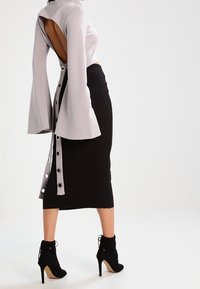 Grå långärmad topp med öppen rygg och trumpetärmar, tillsammans med en svart pennkjol. Svarta ankelskot med hög klack.