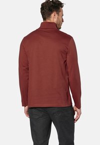 Bordeauxfarbenes Langarmhemd mit hohem Kragen, aus glattem Stoff gefertigt, mit lockerer Passform und kontrastierendem Steppdetail entlang der Nähte.