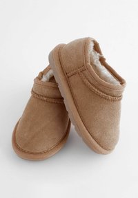 Tan, zachte suède instappers met een pluche interieur, ronde vorm en rubberen zool. Decoratieve stiksels langs de randen.