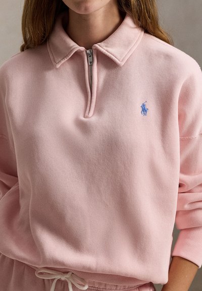 Φούτερ ανοιχτό ροζ με φερμουάρ στον γιακά και ριμπ τελειώματα στα μανίκια. Διαθέτει μικρό μπλε κεντητό λογότυπο στο στήθος και μαλακή υφή.