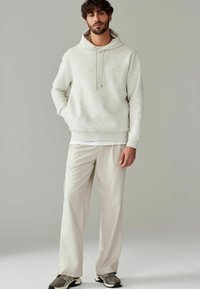 Lys grå hættetrøje med et struktureret mønster, parret med beige plisserede bukser og grå sneakers med sorte detaljer.