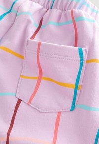 Primo piano di un tessuto rosa con strisce verticali e orizzontali multicolori e una tasca quadrata cucita con motivo coordinato.