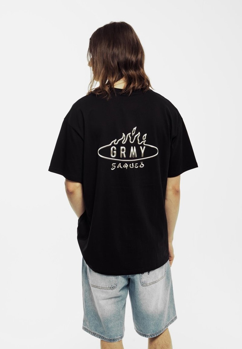 Czarna bawełniana koszulka z białą grafiką z tyłu, na której znajduje się napis "GRMY" w stylizowanym kroju pisma, zestawiona z jasnymi dżinsowymi szortami.