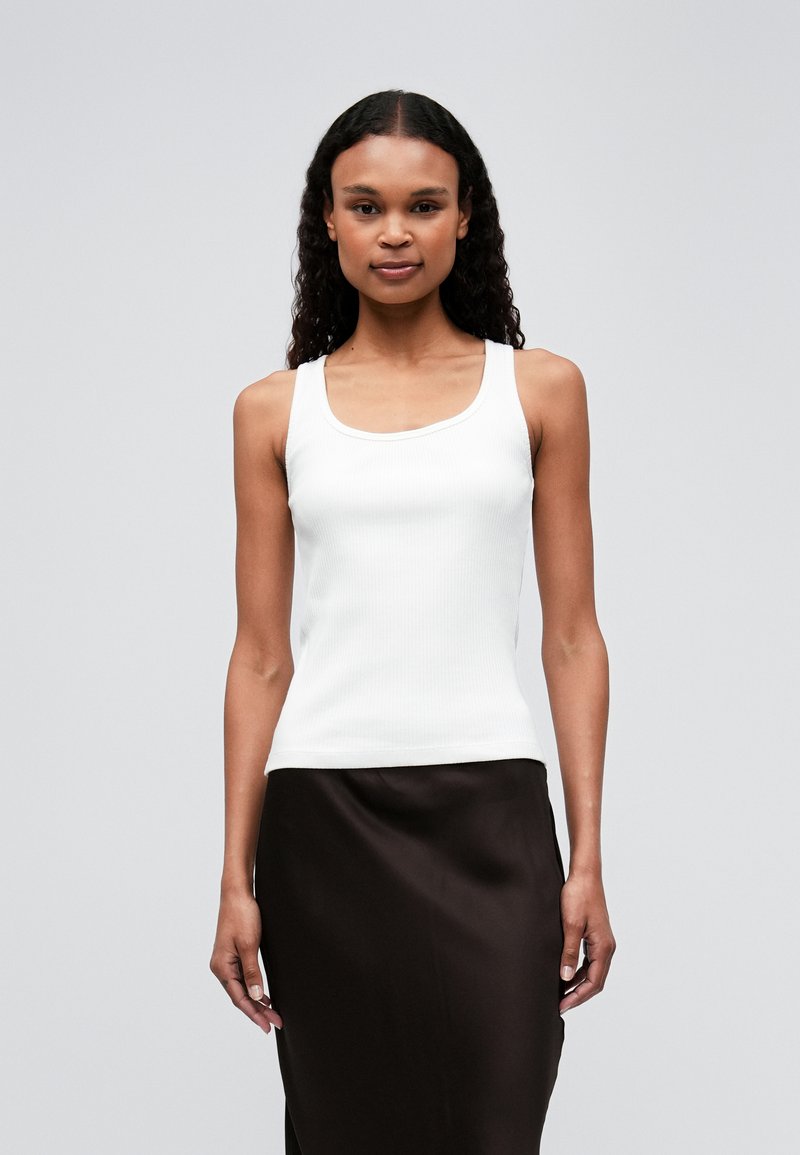Witte geribde tanktop met brede bandjes, met een scoop neckline. Gecombineerd met een gladde, donkerbruine rok. Eenvoudig en getailleerd ontwerp.