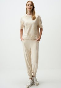 Beige korte mouw top met bloemenpatroon, gecombineerd met bijpassende tapered broek. Textuurstof en elastische boorden. Sneakers maken de outfit compleet.