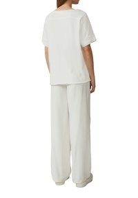 Biała bluzka na krótki rękaw o luźnym kroju, zestawiona z luźnymi białymi spodniami. Gładka tekstura; minimalistyczny design bez widocznych wzorów.