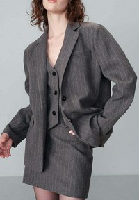 Blazer grigio a righe con gilet abbinato, caratterizzato da una vestibilità su misura, due tasche frontali e bottoni neri. La gonna presenta un motivo simile.