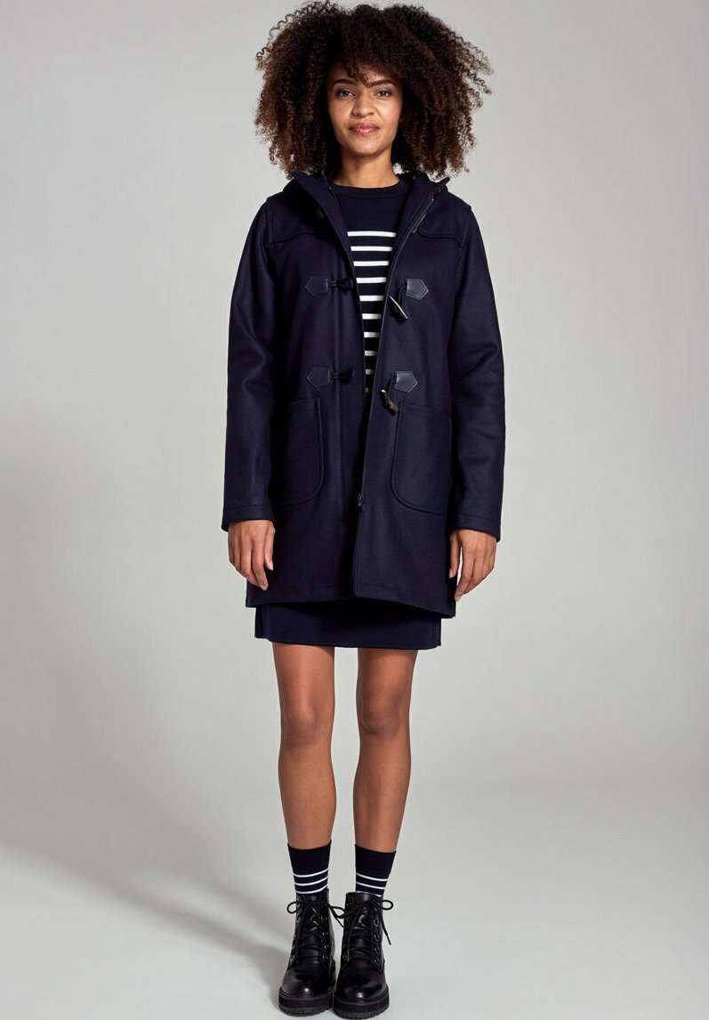 Marineblauwe wollen duffeljas met togglesluiting, twee voorkovacnten en een capuchon, gecombineerd met een gestreepte top en zwarte veterschoenen.
