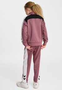 Różowy i czarny dres z białymi paskami po bokach i wzorami w chevrons, wykonany z miękkiego materiału, z wysokim kołnierzem i mankietami.
