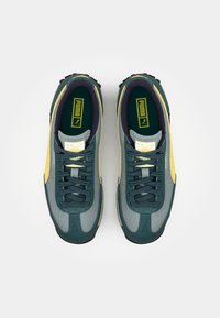 Teal ja kollase Puma tossupaar mustade nööridega vaadatuna ülalt valgel taustal.