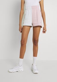 Růžové a bílé kraťasy s blokovým vzorem, elastickým pasem, bočními kapsami a logem Nike. Nosit je s bílými teniskami a ponožkami.