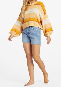 Stickad tröja i orange, gult och vitt randigt mönster med puffärmar, i kombination med ljusblå denimshorts med fransad nederkant.